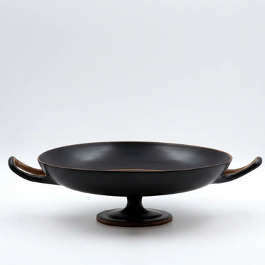 Hand-thrown black ceramic kylix bowl with two handles and pedestal base on white background