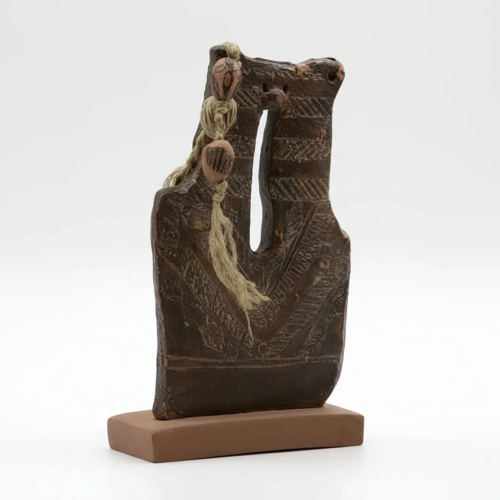 A dark-colored, textured plaque with a rope-like twine attached, possibly made of wood or stone, displayed on a small brown stand.