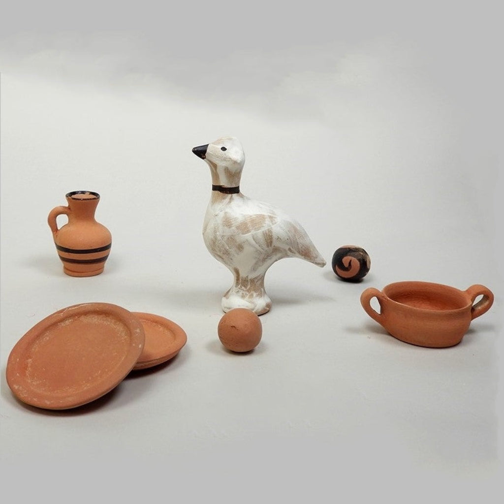 A collection of ancient Greek toy replicas including a bird figurine, a cooking pot, plates, and two ceramic marbles.