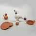 A collection of ancient Greek toy replicas including a bird figurine, a cooking pot, plates, and two ceramic marbles.
