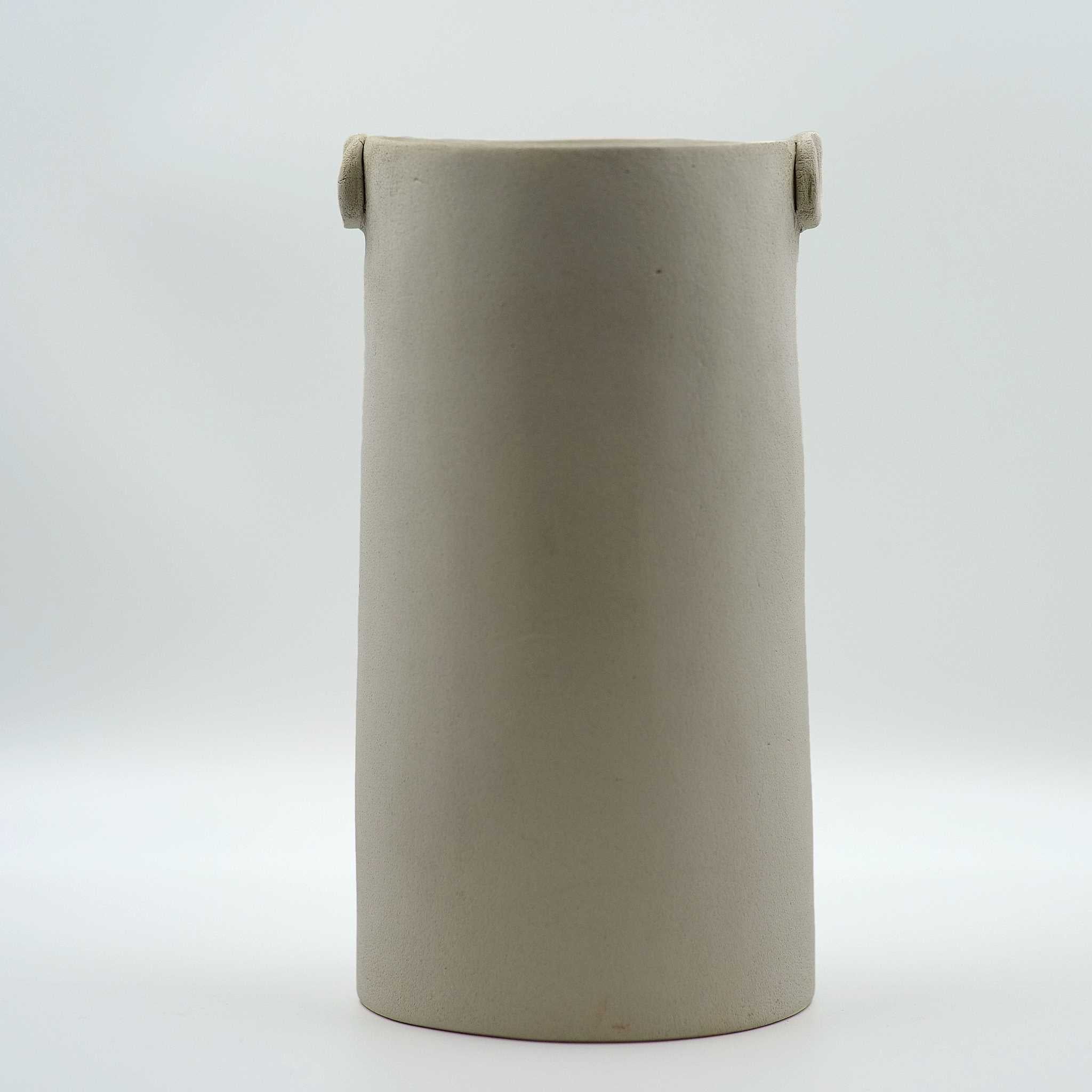 A hand-built cylindrical stoneware vase with a grayish-white color and attached knob-like handles near the rim.