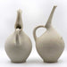 Two beige, hand-built ceramic jugs with a subtle breast-like swell and a spout, crafted in glazed stoneware.