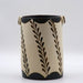 A cylindrical ceramic vase with a geometric pattern featuring leaves in beige, black, and gold colors.