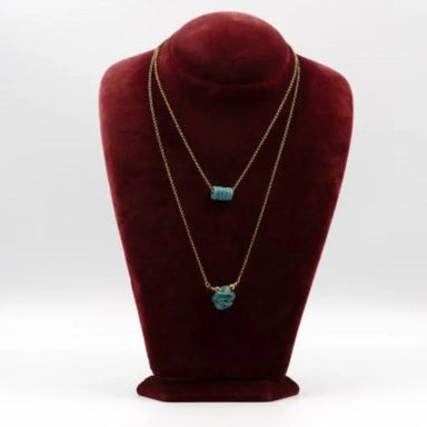 Gold necklaces with turquoise pendants on a red velvet stand.