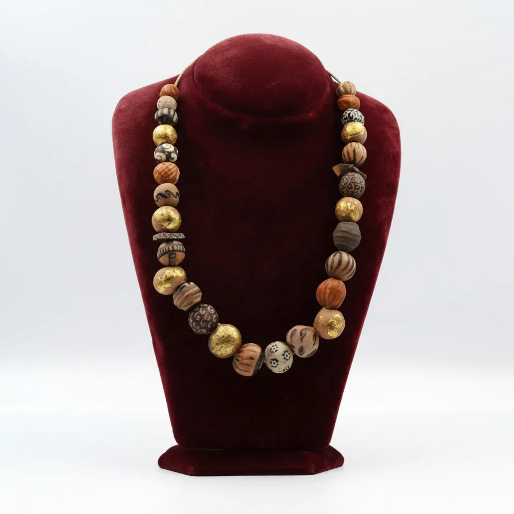 A ceramic bead necklace displayed on a red velvet stand, featuring a variety of earthy tones.