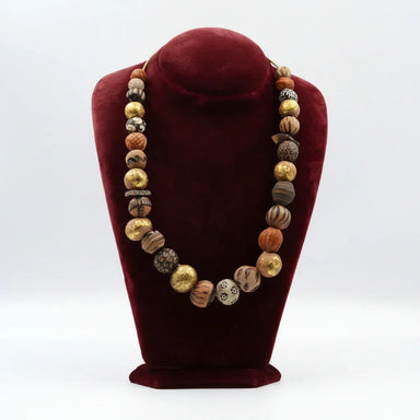 A ceramic bead necklace displayed on a red velvet stand, featuring a variety of earthy tones.
