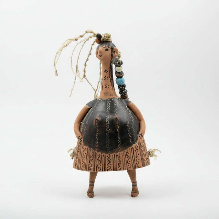 A bell-shaped ceramic doll with painted decoration, featuring a neck, head, and hands attached to the body. The doll is standing against a gray background.