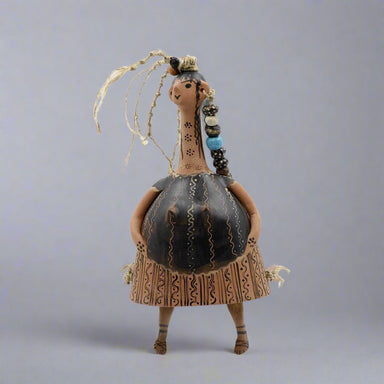 A bell-shaped ceramic doll with painted decoration, featuring a neck, head, and hands attached to the body. The doll is standing against a gray background.