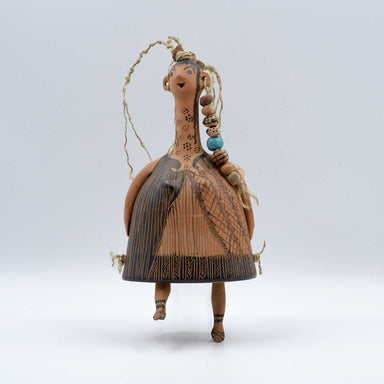 A bell-shaped plangona doll with painted decoration, featuring a neck, head, and hands attached to a wheel-thrown ellipse body. The doll is adorned with polychrome threads and beads.