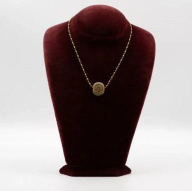 A plastic and ceramic pendant with a gold-tone chain, displayed on a maroon-colored mannequin bust.