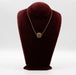 A plastic and ceramic pendant with a gold-tone chain, displayed on a maroon-colored mannequin bust.