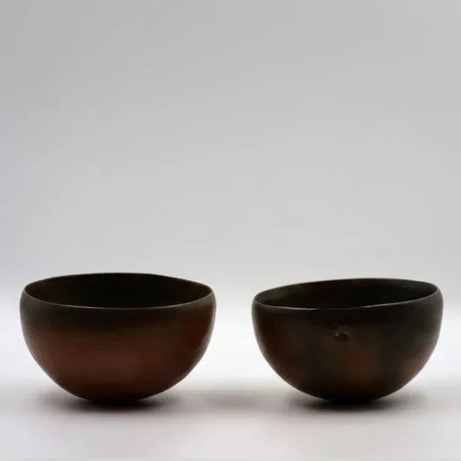 Two hemispherical brown ceramic bowls placed one in front of the other on a plain background.