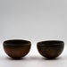 Two hemispherical brown ceramic bowls placed one in front of the other on a plain background.